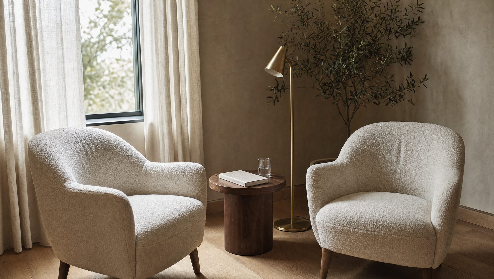 Two cream armchairs and a small table in the consultation corner, morning light through linen curtains